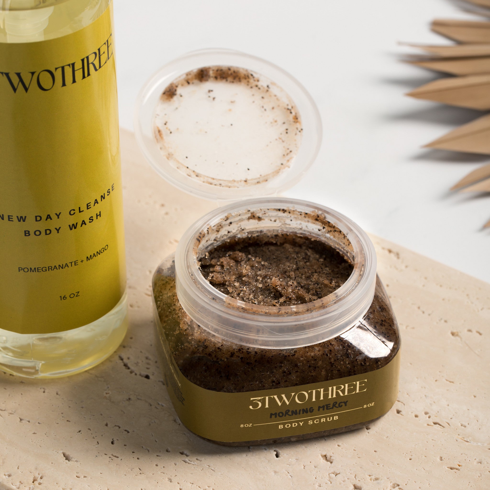close up of Morning Mercy Body Scrub square plastic jar with open, showing the texture of the body scrub, bottle of body wash in the left corner background. New Day Cleanse Body Wash and the Morning Mercy Body Wash are a perfect duo for a fresh daily reset. 