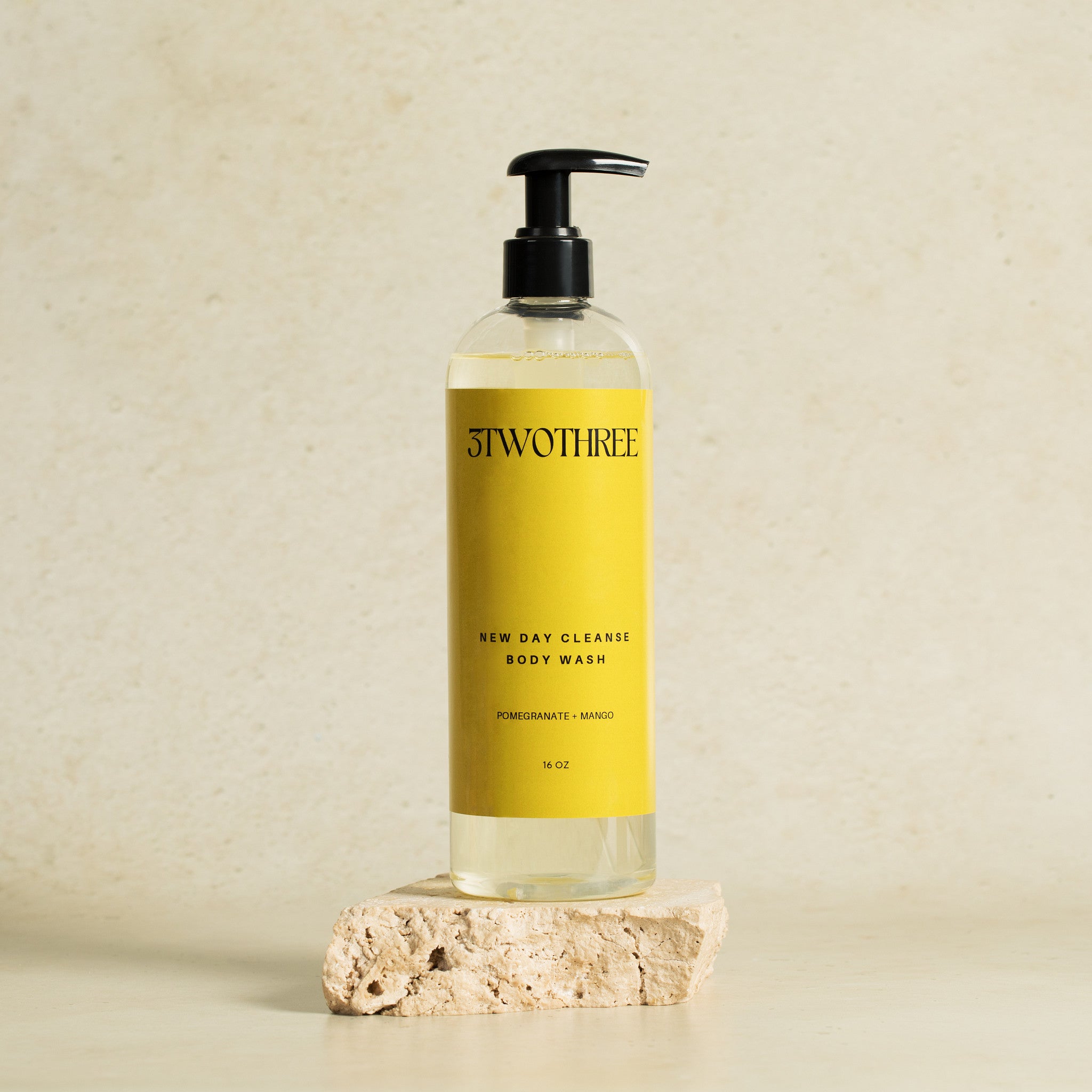  Bottle of '3TwoThree' New Day Cleanse body wash on a beige background, 16 oz Clear plastic Bottle with black pump, yellow label with black print.