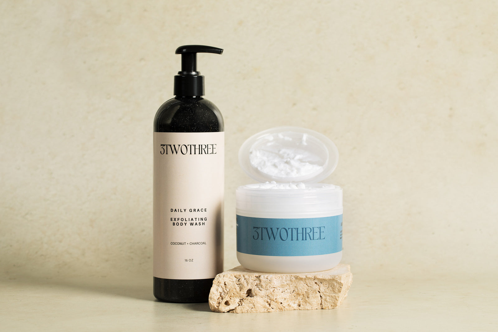 Two skincare products (Daily Grace Exfoliating Body Wash and Daybreak Whipped Body Butter) from the brand '3TWOTHREE' on a beige background