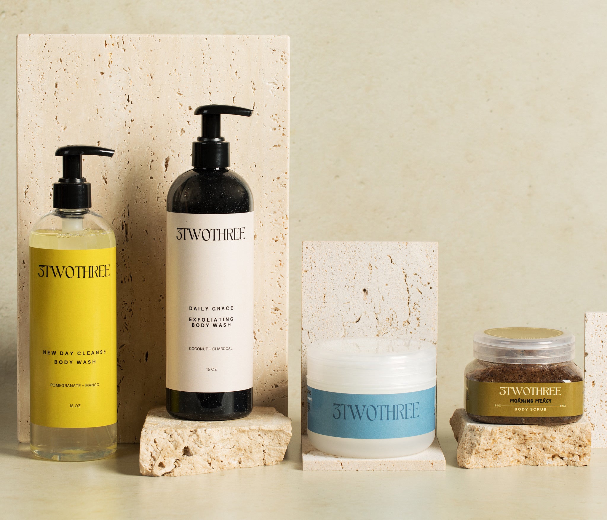Four 3TWOTHREE body skincare products on a neutral background (New Day Cleanse Body Wash, Daily Grace Exfoliating Body Wash, Daybreak Body Butter, Morning Mercy Body Scrub)